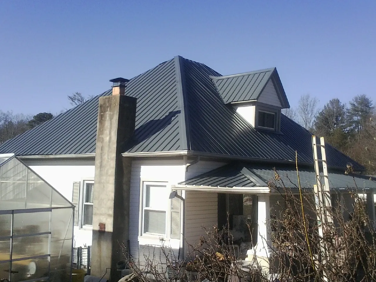 Dark blue standing seam metal roof on a white farmhouse with dormer — Slate & Tile Roof Repair by Roofing Brothers in Iron Station