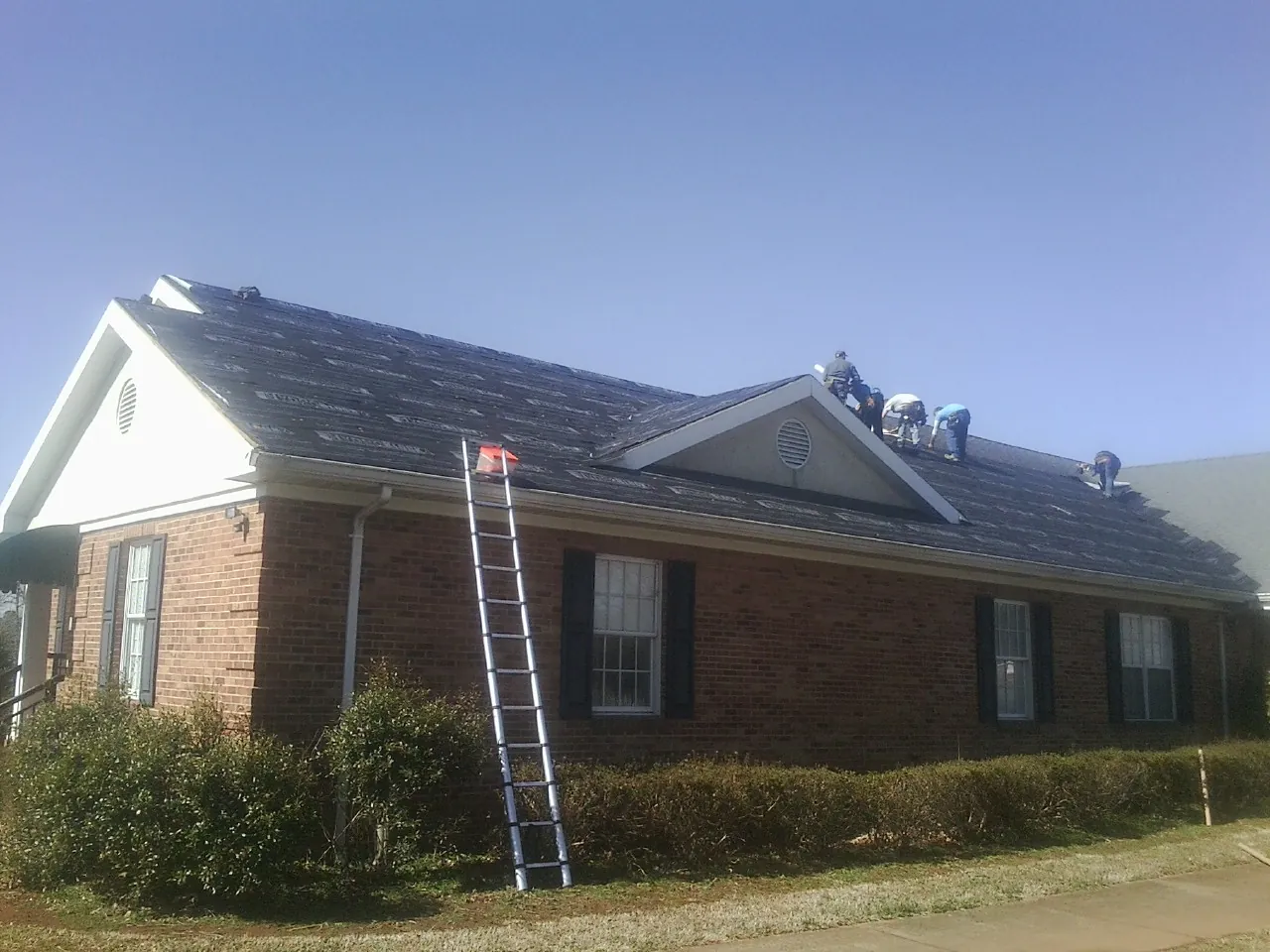 Crew tearing shingles off a brick ranch roof with a ladder set — Metal Roof Repair work by our crew in Iron Station