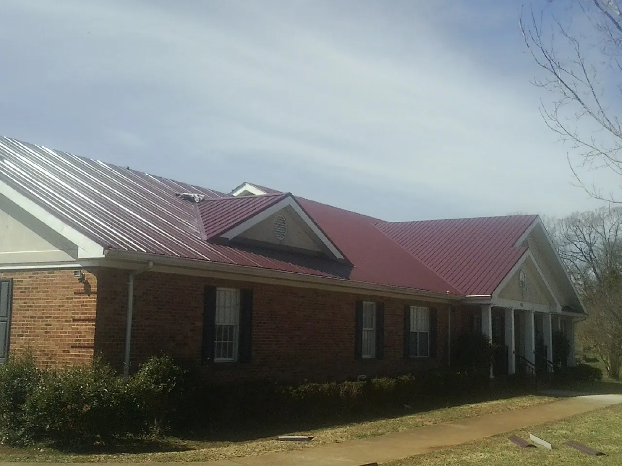 Red metal roof with gabled entries on a long brick building, from a Hail Damage Roof Repair job in Iron Station
