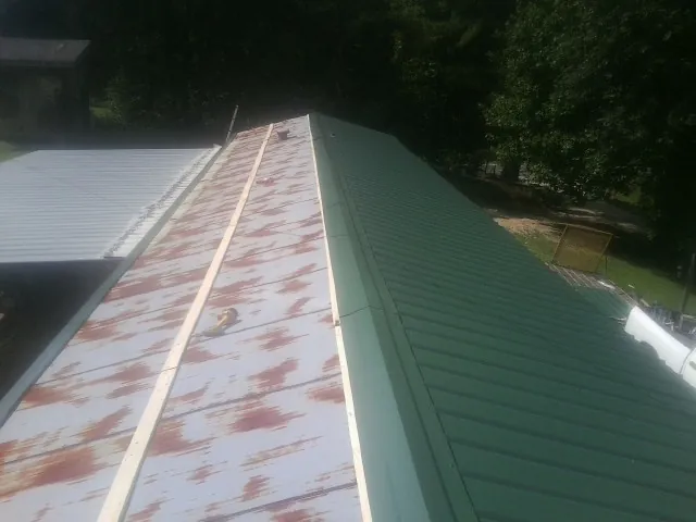 Old rusted panels beside newly installed green metal roofing — Wind Damage Roof Repair by Roofing Brothers in Iron Station