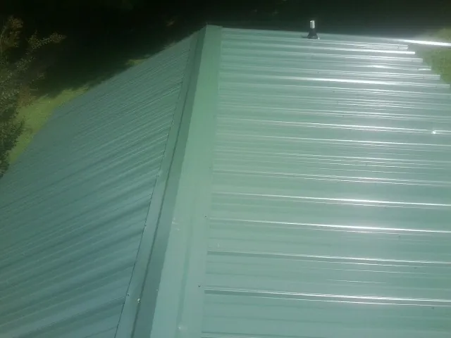 New green metal panels meeting at the ridge of a roof — Flat Roof Repair work by our crew in Iron Station