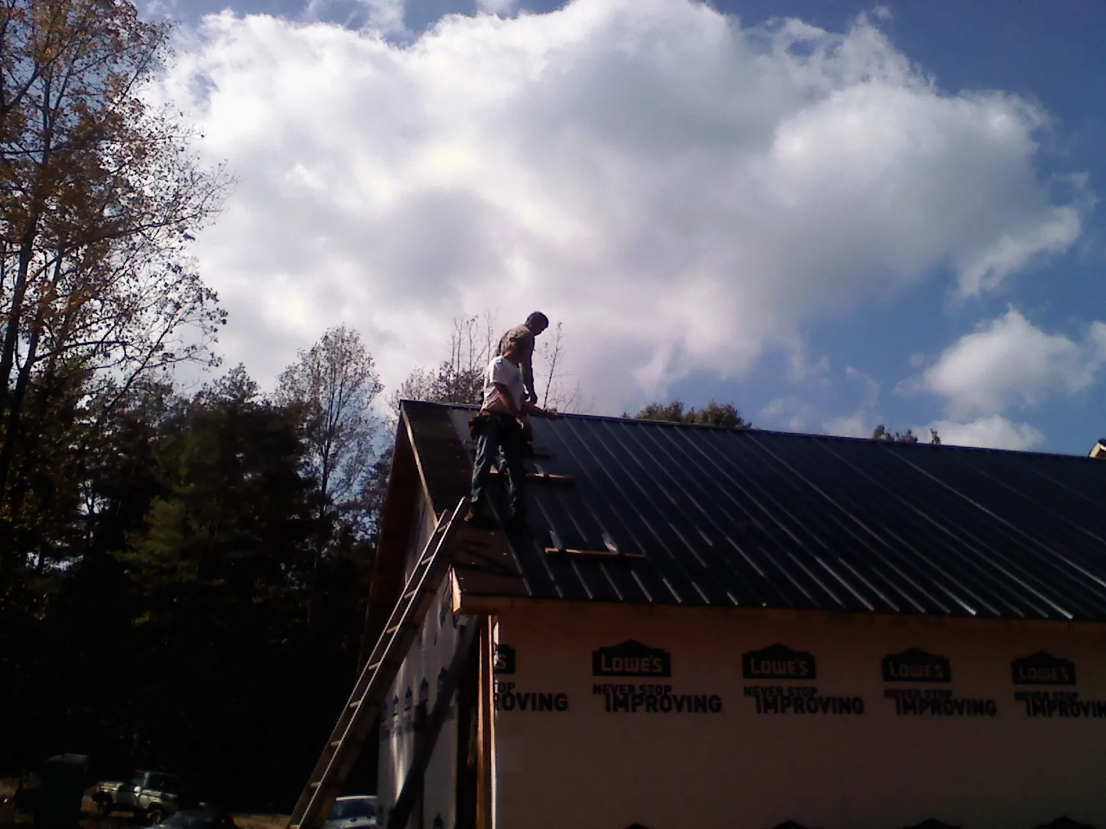 Roofer fastening dark metal panels high against a cloudy sky, from a Roof Inspection job in Iron Station