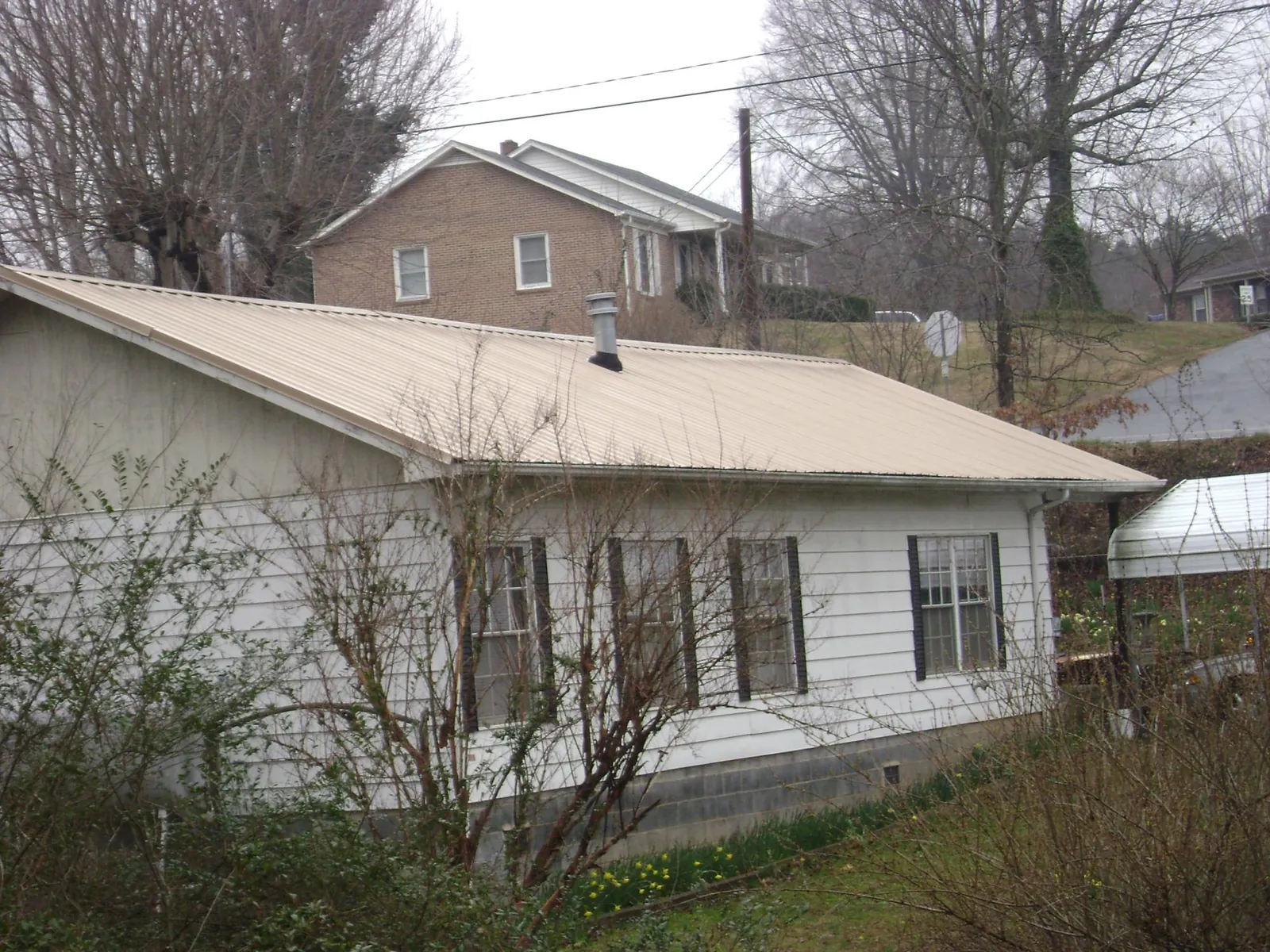Tan metal roof on a white sided house set into a hillside — Commercial Roofing by Roofing Brothers in Iron Station