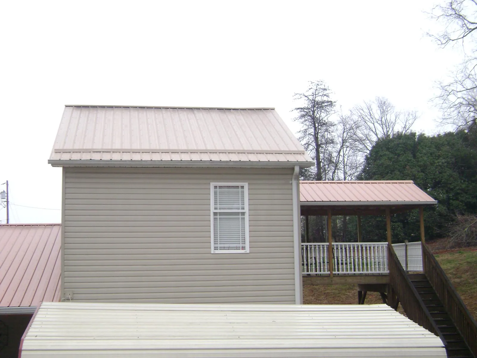Tan metal roofs on a two story addition and attached porch, from a Roof Replacement job in Iron Station